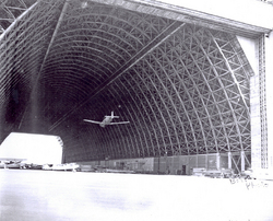 Airplane flying through open hangar bay at Naval Air Station Til